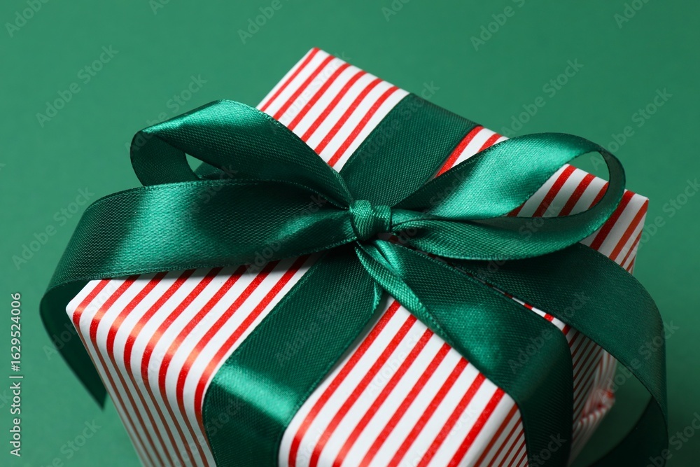 Fototapeta premium Close up of beautiful Christmas gift with red ribbon on green background, top view, space for text
