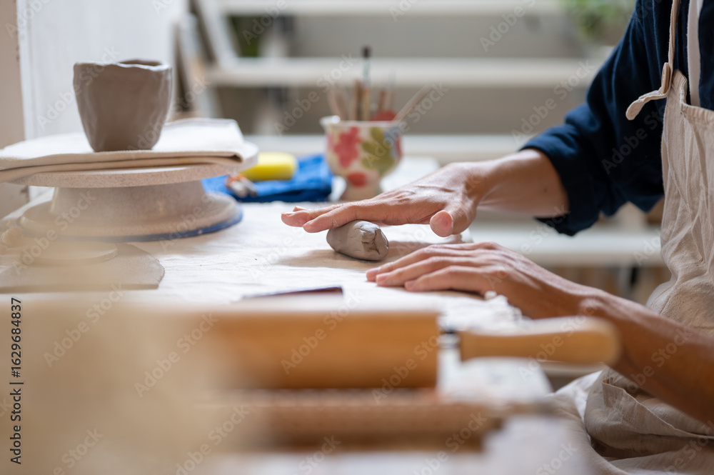 Fototapeta premium Close up of pottery artist's hand molding a clay mug's handle at working table in a class or studio.