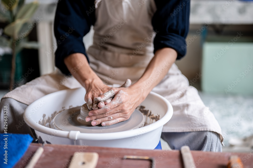 Close up of pottery artist's stained hands molding up a clay on throwing wheel in a class or studio. Close up of pottery artist's stained hands molding up a clay on throwing wheel in a class or studio.