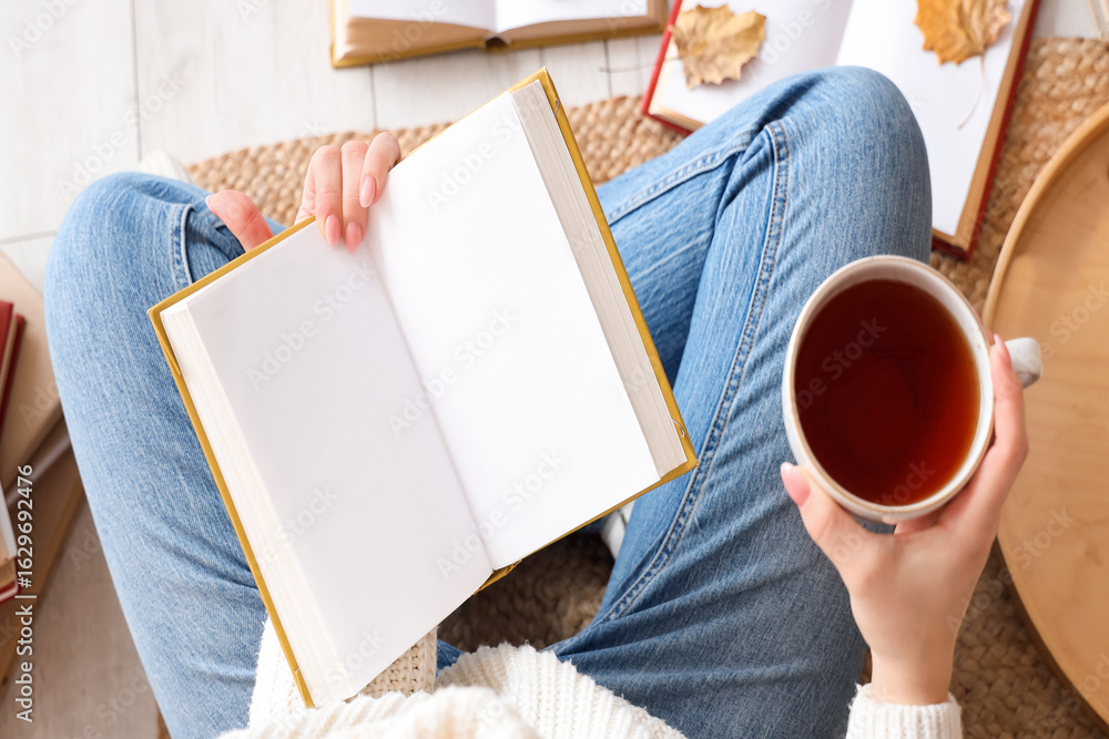 Obraz premium Woman with blank book and cup of tea sitting on rug at home, top view