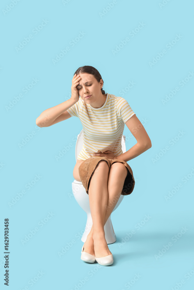 Fototapeta premium Young woman suffering from cystitis on toilet bowl against blue background