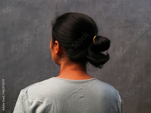 Asian Indonesian woman, seen from behind, is putting her hair up with a focused and casual gesture.