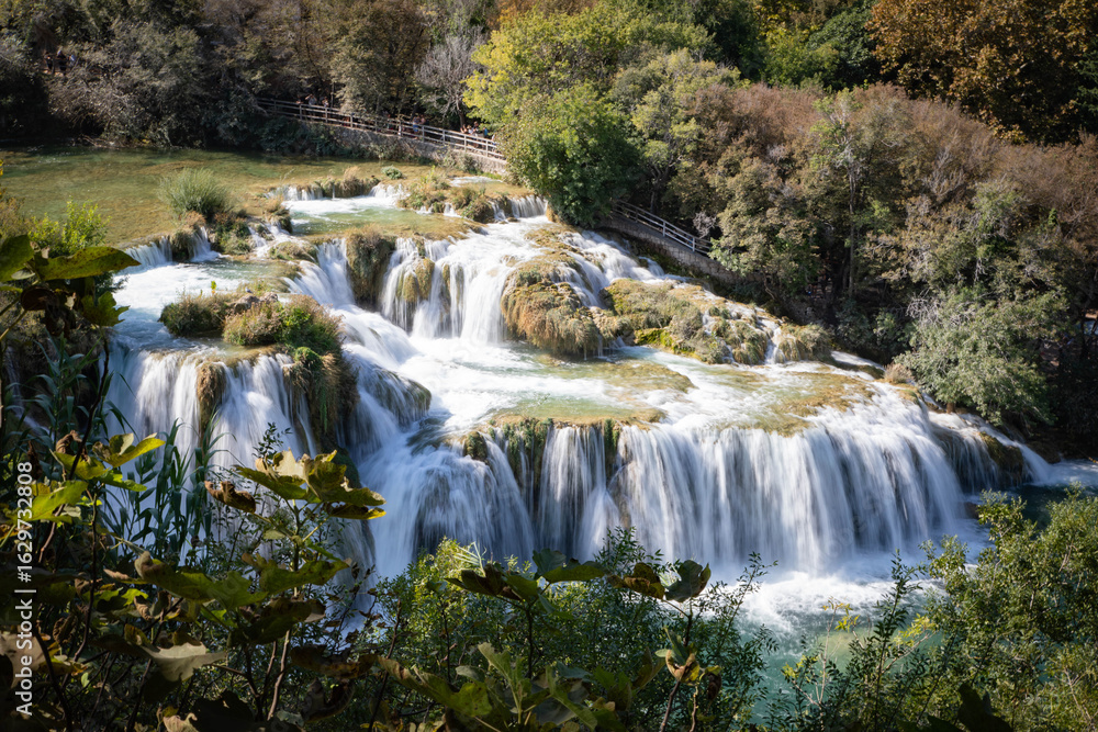 Obraz premium Peaceful waterfall in a Croatian national park surrounded by lush greenery and clear water. A stunning natural landscape ideal for travel, nature, adventure, and outdoor-themed content