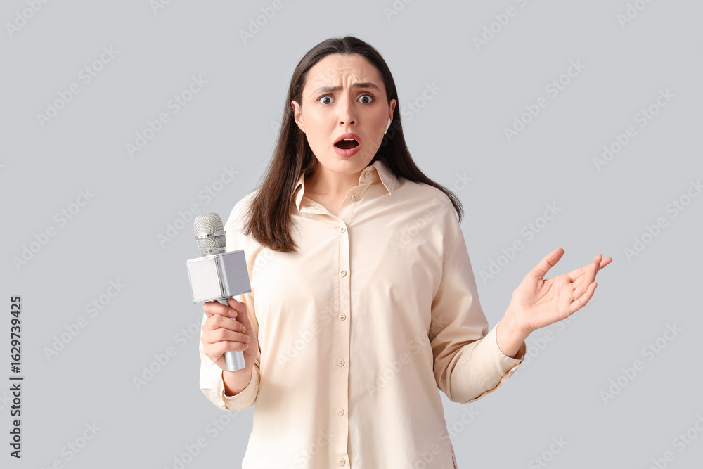 Shocked female reporter in earphone with microphone on light background Shocked female reporter in earphone with microphone on light background