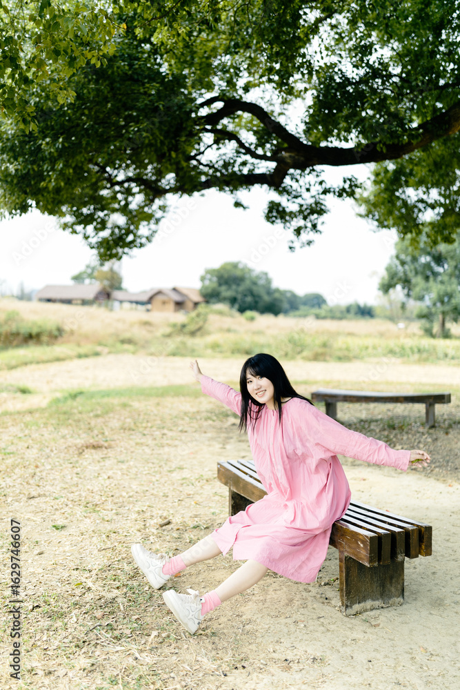 Naklejka premium Young Asian woman in pink dress sitting on a bench outdoors.