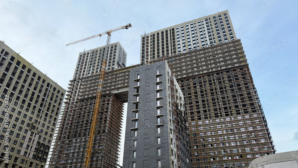 Fototapeta premium Construction site of two tall residential buildings under development, with scaffolding and crane, showcasing the modern building process and urban architecture in progress