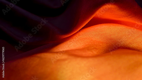 Close-up view of flowing orange and dark fabric with soft folds.