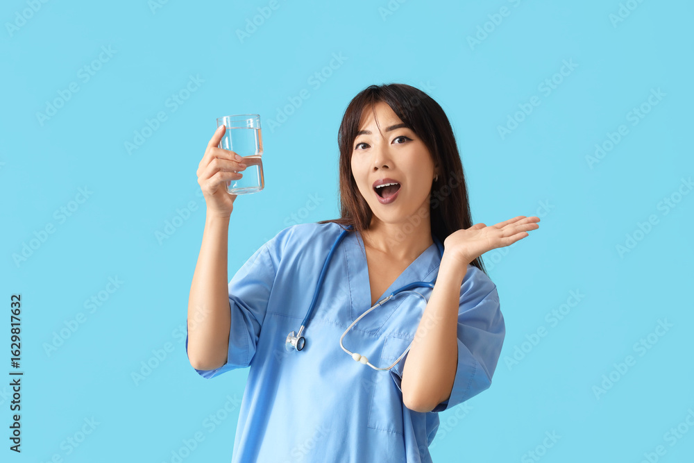 Happy female Asian doctor with glass of water on blue background Happy female Asian doctor with glass of water on blue background