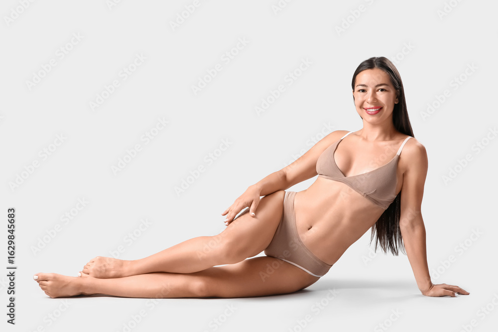 Fototapeta premium Young woman in underwear with cellulite problem lying on light background