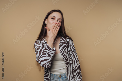 portrait of young cheerful woman in a zebra print shirt blowing a kiss, showcasing joy and liveliness on calm yellow background