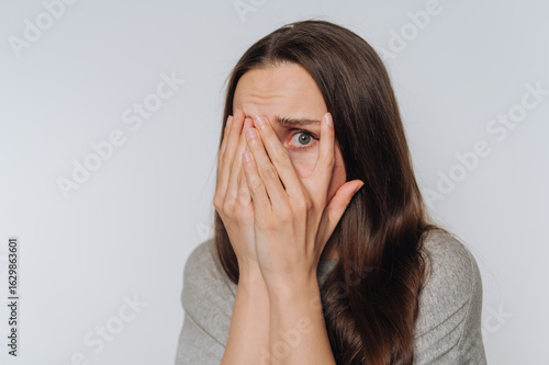 Wallpaper Mural portrait of young fearful woman covers her face with her hands, showing vulnerability and internal struggle on light background Torontodigital.ca