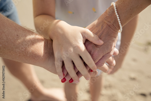 Drei Generationen halten sich an den Händen am Strand – Symbol für Familie, Zusammenhalt und Liebe