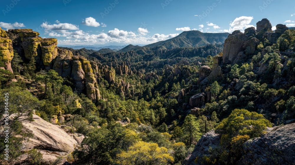 Naklejka premium Panoramic view of rugged mountains, dense forests, and scattered clouds under a vibrant blue sky