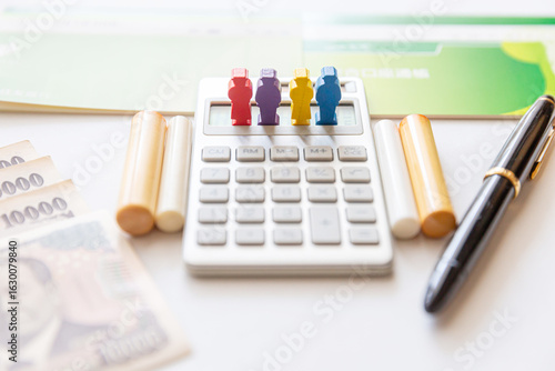 Photos 家族 親族、複数の通帳と印鑑、計算機、紙幣によるお金イメージ 財産分与、遺産相続のイメージ