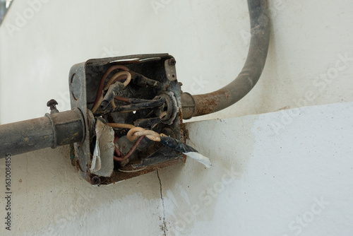 Old rusty electrical junction box on a concrete wall, The box is open and has several exposed electrical wires and several conduits running into the box.