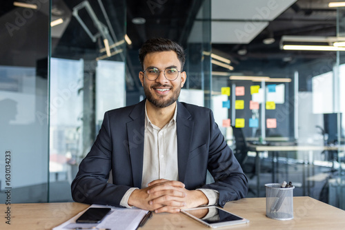 фотографія A smiling businessman sits at a desk in a modern office