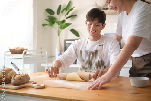 Photos Happy couple enjoying baking at home, flattening dough with a rolling pin
