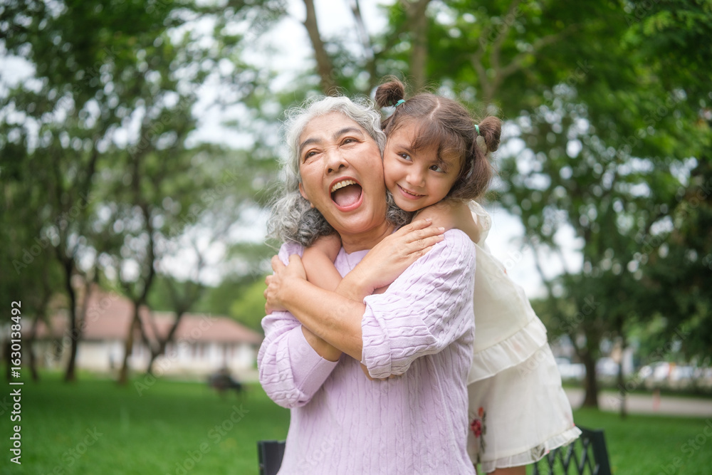 Fototapeta premium Elderly woman enjoying an affectionate embrace from her young granddaughter during outdoor family time.