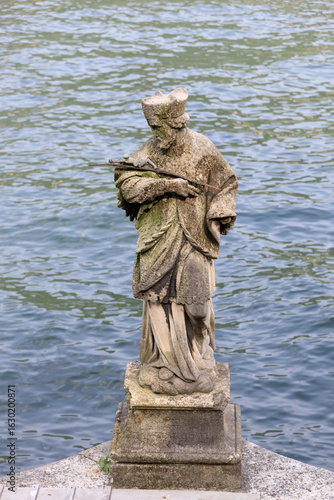 Old weathered stone statue of a saint by the lakeside in Como, Italy
