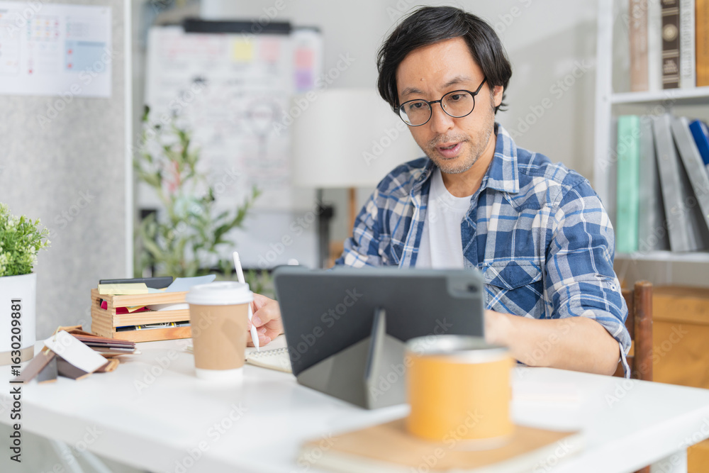 Cheerful Asian businessman with positive thinking and confidence sits at her desk, working in a modern home studio with her partners. he concentrates on their creative vision in the bright daylight Cheerful Asian businessman with positive thinking and confidence sits at her desk, working in a modern home studio with her partners. he concentrates on their creative vision in the bright daylight