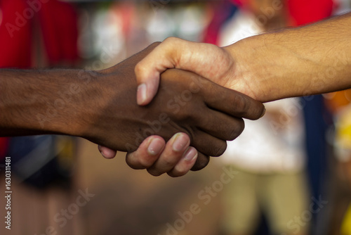 A white boy and a black boy are shaking hands and the background behind them is blurred.