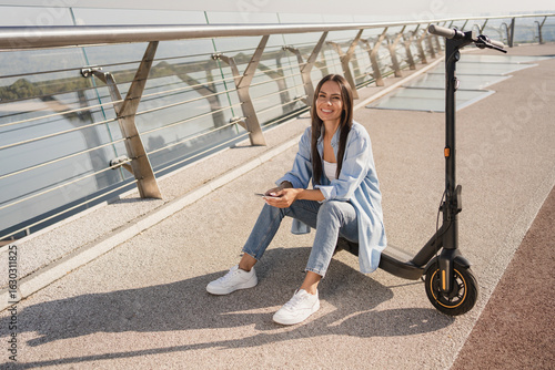 Smiling woman holding smartphone using mobile app for electric scooter rental while has excursion traveling exploring riding in the city center. Eco Transportation green ecology sustainable concept
