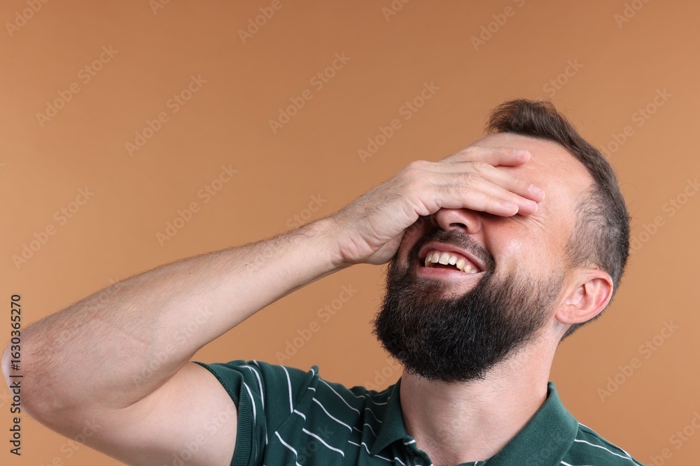 Obraz premium Man covering eyes and laughing on brown background
