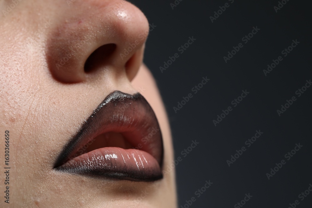 Fototapeta premium Beautiful young woman with black lip liner on dark grey background, closeup. Space for text