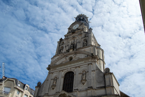 French ecclesiastical heritage: Low angle view of the belfry and clock tower of Église Sainte-Croix under a cloudy sky in Nantes, France.