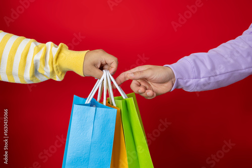 Female hand handing multicolored shopping bags to a customer on a red background, shopping concept