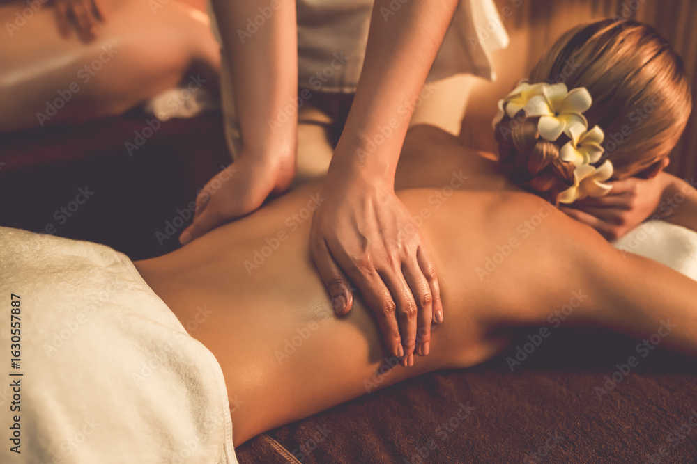 Obraz premium Closeup couple customer enjoying relaxing anti-stress spa massage and pampering with beauty skin recreation leisure in warm candle lighting ambient salon spa at luxury resort or hotel. Quiescent