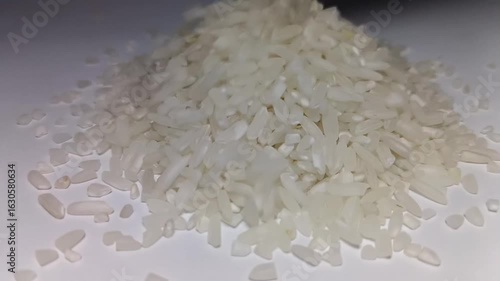A macro close-up shot of a pile of raw, uncooked white rice grains on a clean white background with subtle lighting