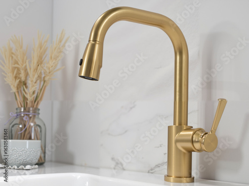 Modern gold kitchen faucet on countertop with marble backdrop  