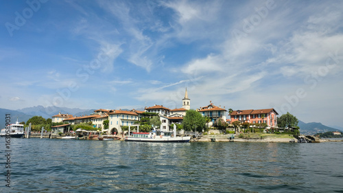 Photos Isola Superiore (Isola dei Pescatori), Italy: A scenic view of the picturesque island on Lake Maggiore, with historic buildings, a prominent bell tower, and ferries docked at the shore