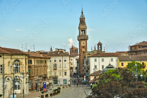 Casale Monferrato, Italy: The historic Torre Civica (Civic Tower) rises above a bustling city square surrounded by traditional Italian architecture.