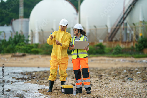 Workers conduct environmental assessment near industrial site on coastal shore during daylight hours