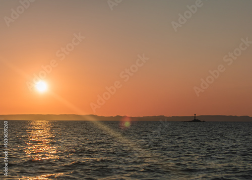 Sunset Over Ocean with Distant Lighthouse Beacon and Mountain Horizon