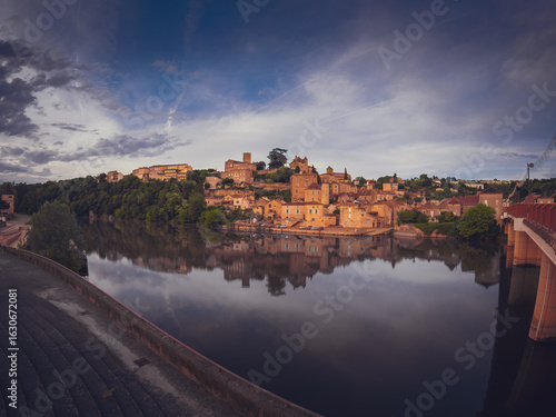 Panoramic view of the medieval village of Puy-l'Évêque, located on the banks of the Lot River in the Occitanie region of southwestern France. Traditional stone houses and historic buildings reflect in