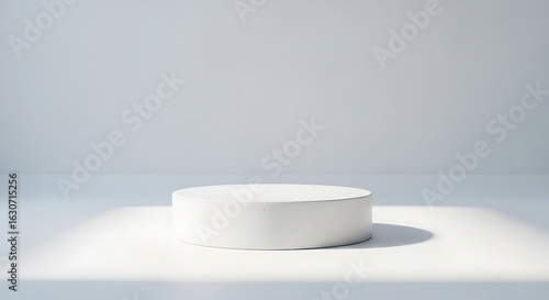 Minimalist white cylinder pedestal illuminated by a soft spotlight on a light gray textured background for product display