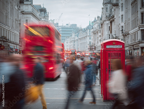 Iconic city scene featuring a vibrant red telephone booth amidst blurred motion of bustling street life and a doubledecker bus. Evokes travel, culture, and urban energy.