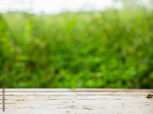 A wooden table with a grassy background. The grass is green and the table is empty. Selective focus. Scene in rural country side. Summer time vibe.