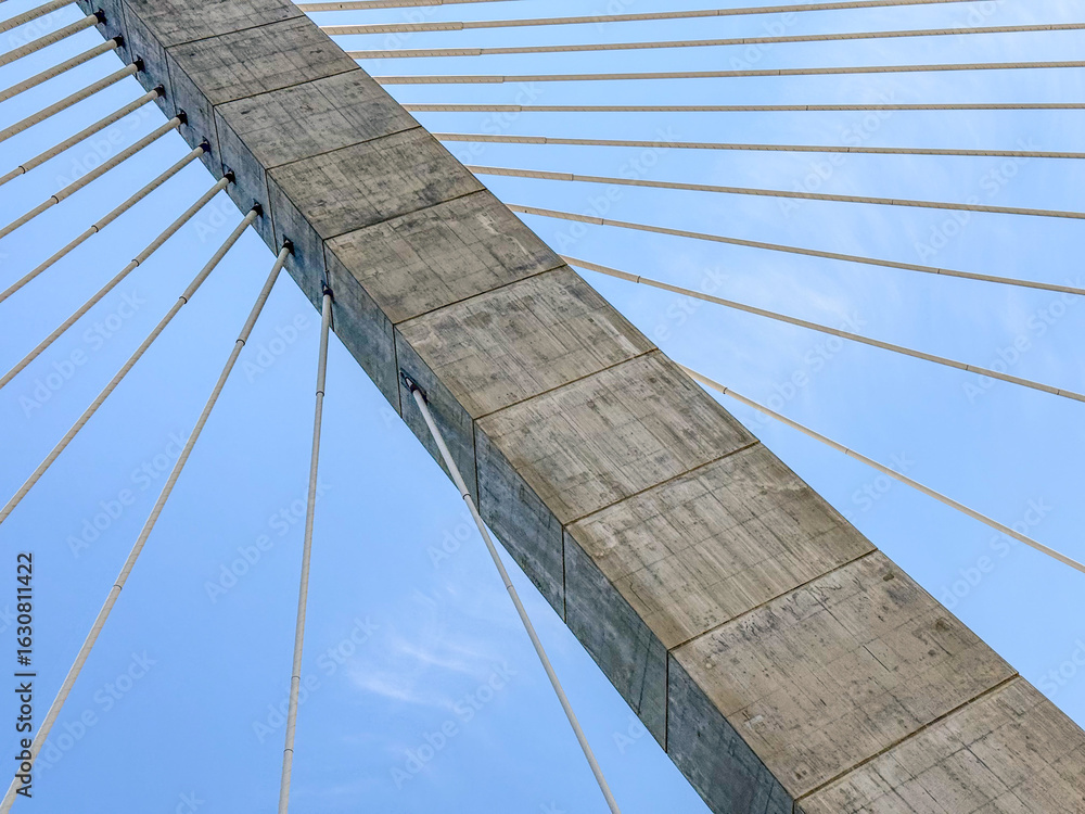 Obraz premium Cables on a suspension bridge connected to a cement anchor column on a blue sky day