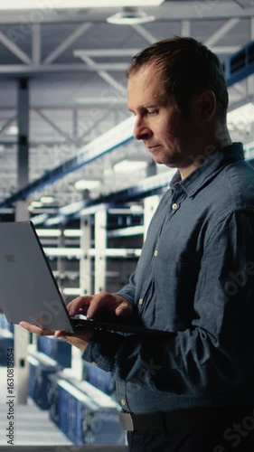 Wallpaper Mural Vertical video Technician monitors server room activity using laptop while walking through facility. Data center IT professional reviews rigs tests results to ensure systems are working correctly Torontodigital.ca