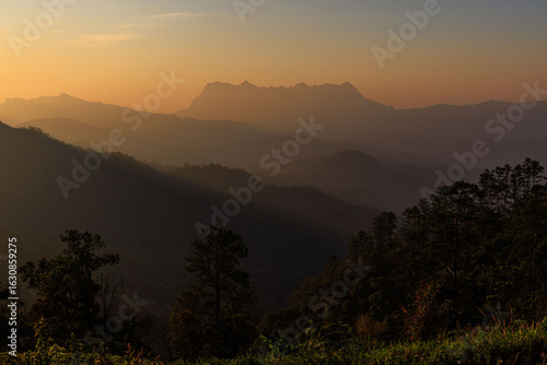 The sky is a beautiful orange color, and the mountains are covered in trees, Chiang Dao, Thailand