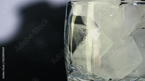 Orange Beverage Poured in Glass with Ice Cubes.  Glass rotating in slow motion. Soft Lighting on Dark Background