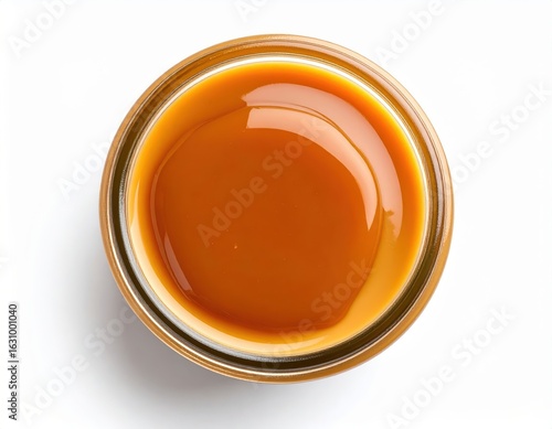 Close-up top view of a small glass jar filled with smooth glossy caramel sauce on a white background with reflection and lighting details