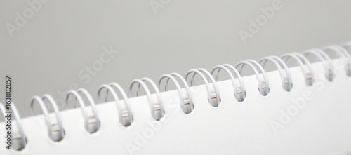 A close-up, abstract shot of the white plastic spiral binding of a notebook or calendar against a simple, light gray background. The focus is on the repeating rings.