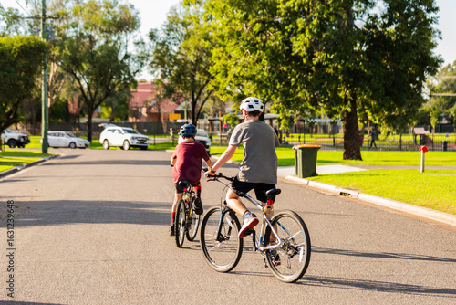 Young Aussie brothers on bikes with helmets riding away on road in country town