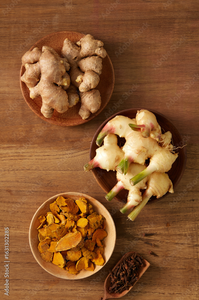 Fototapeta premium Flat lay of fresh ginger and sliced turmeric on a dark wood table. A rustic and bold color palette creates an earthy, herbal aesthetic ideal for traditional medicine, essential oils, herbal visuals.