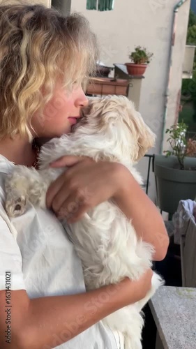 Smiling child joyfully embraces a fluffy white puppy indoors. The child shows happiness and affection while holding the adorable, playful dog close. The moment captures warmth and friendship